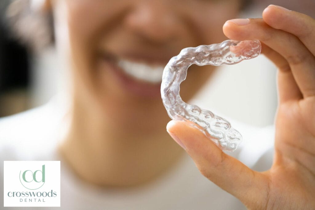 The woman holds in her hand removable invisible transparent aligners and smiles